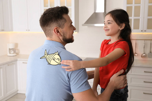 Cute little girl sticking paper fish to father's back at home - Fotografie, Obrázek
