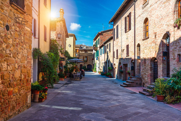 Cozy street decorated with colorful flowers, Pienza, Tuscany, Italy, Europe. Narrow street in the charming town of Pienza in Tuscany. Beautiful streets of the small and historic village Pienza, Italy - Фото, изображение
