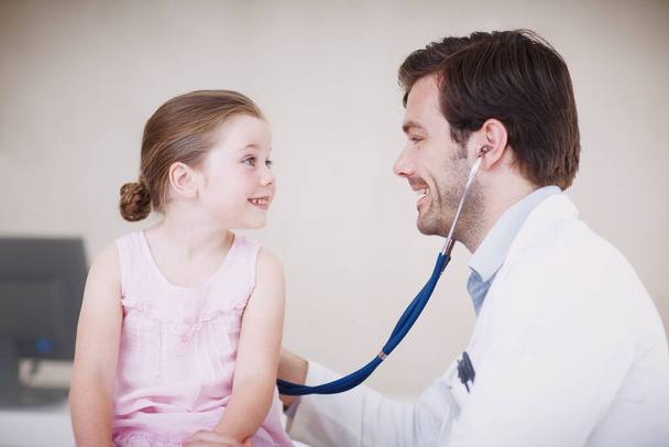 Ти в ідеальній формі. Чоловік лікар вивчає маленьку дівчинку зі стетоскопом
 - Фото, зображення