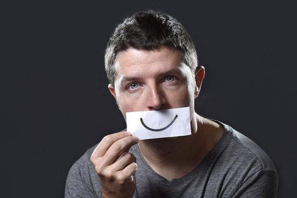 молодий депресивний чоловік втратив смуток і печаль тримаючи папір з усмішкою на роті в концепції депресії
 - Фото, зображення