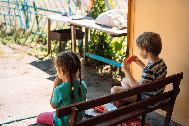 Children sitting on a bench eat watermelon. - Foto, Bild