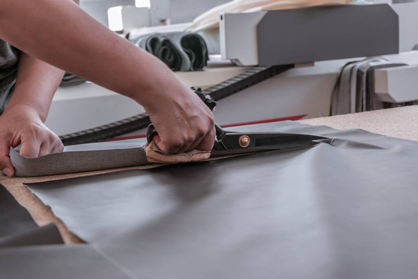 A cutter cuts fabric with scissors in a sewing workshop - Foto, afbeelding