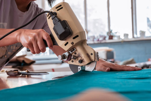 The cutter cuts the fabric with a disc knife in a sewing workshop - Fotó, kép
