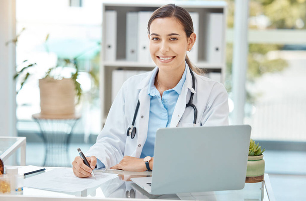 Healthcare, medicine and a doctor writing on insurance document or patient file. Happy woman working in medical field, at desk with laptop consulting online and filling in a script at hospital office. - Zdjęcie, obraz