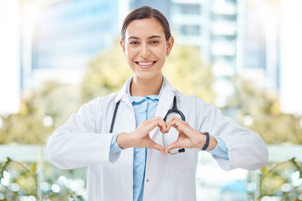 Χαμόγελο ιατρός με την καρδιά σημάδι χέρι χειρονομία στη σύγχρονη κλινική υγείας ή νοσοκομείο. Ευτυχής, θετική και ευεξία νεαρή γυναίκα εργαζόμενος υγειονομικής περίθαλψης ή γιατρός με την υποστήριξη, την αγάπη και το σύμβολο φροντίδας. - Φωτογραφία, εικόνα