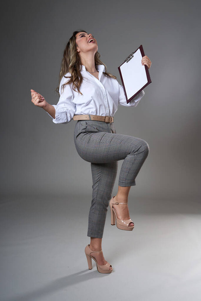 Full length portrait of a young attractive businesswoman with a clipboard and documents, studio shot on gray background - Fotoğraf, Görsel