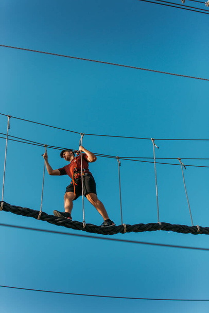 Jonge atletische jongen op de enkele touwbrug in het avonturenpark - Foto, afbeelding