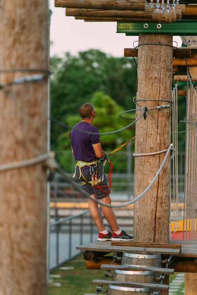 Aventure homme levant les yeux tout en se tenant près des piliers en bois au parc d'aventure - Photo, image