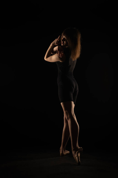 Silhouette of ballerina posing from the back while bending - Foto, afbeelding