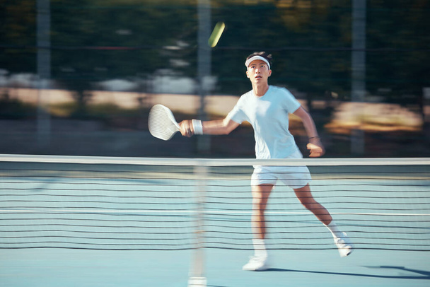 Asian tennis professional training with a racket and playing a game on court. Fit athlete running during a match and play competitive sport workout for fitness and health alone in a sports club. - 写真・画像