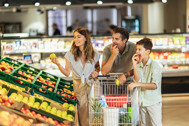 Szczęśliwa rodzina z dzieckiem i wózkiem zakupowym kupując żywność w sklepie spożywczym lub supermarkecie - Zdjęcie, obraz