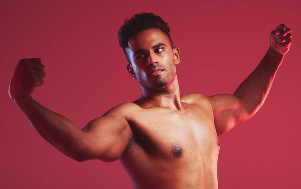 Bodybuilder, μυς και φυσική κατάσταση με ένα γυμνό άνδρα μοντέλο θέτουν shirtless στο στούντιο με ένα κόκκινο φόντο. Γυμνός, δυνατός αρσιβαρίστας με υγιή ανδρικά χέρια που λυγίζουν εσωτερικά για υγεία και ευεξία. - Φωτογραφία, εικόνα