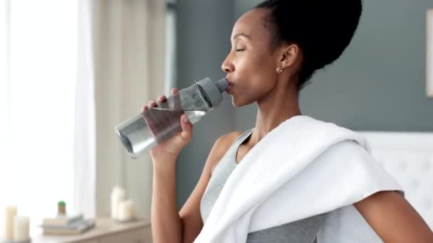 Μπουκαλάκι νερού, ενυδατωμένη και διψασμένη γυναίκα γυμναστικής που πίνει μετά από προπόνηση ή άσκηση ρουτίνας στο σαλόνι της. Μαύρη γυναίκα πίνει φρέσκο, δροσερό και ενυδάτωση h2o για την υγεία. - Πλάνα, βίντεο
