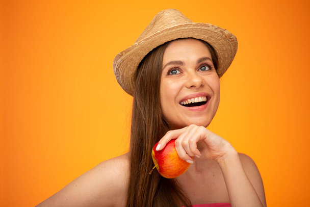 Smiling woman in straw hat holding red apple looking up, face girl portrait isolated over orange yellow background. - Φωτογραφία, εικόνα