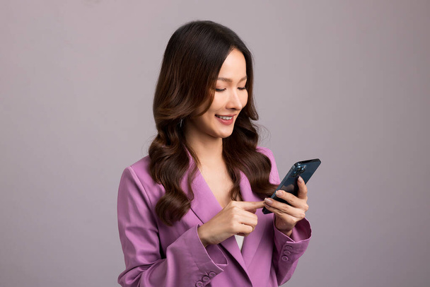 Beautiful Asian womaa using smartphone standing isolated on gray background. Shopping online mobile phone. - Foto, Bild
