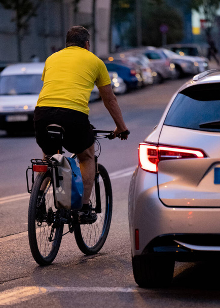 Cyclist overtaking car in a a road with low light. Rider in a risky or danger situation. rear view - Foto, Imagem