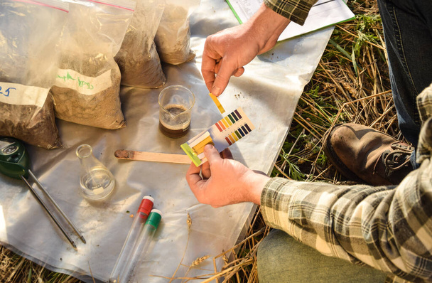 Male agronomy specialist testing soil sample outdoors, using laboratory equipment, performing soil certification at agricultural grain field sunrise. Environment research, soil certification - Fotoğraf, Görsel