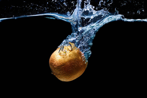 Whole kiwifruit dropped in water with splashes isolated on black background - 写真・画像