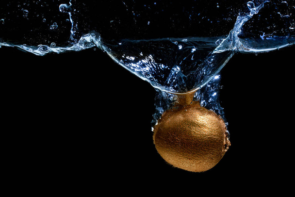 Close-up of a whole kiwi dropped in water with splashes on black - Foto, Imagem