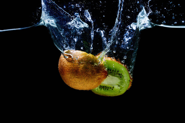 Cut-in-half kiwifruit dropped in water with splashes isolated on black background - Foto, Bild