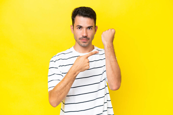 Young handsome man over isolated yellow background making the gesture of being late - Photo, Image