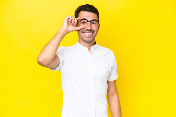 Young handsome man over isolated yellow background showing ok sign with fingers - Zdjęcie, obraz