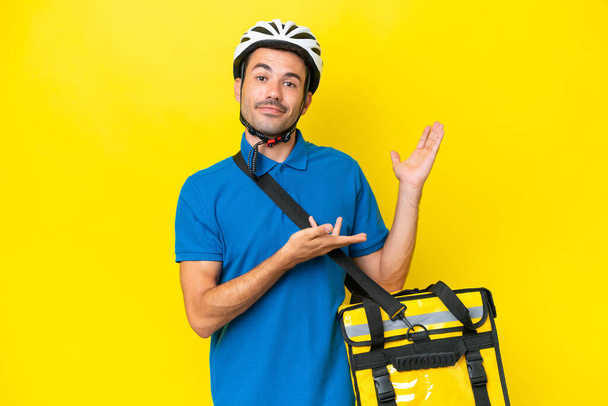 Young handsome man with thermal backpack over isolated yellow background extending hands to the side for inviting to come - Photo, Image