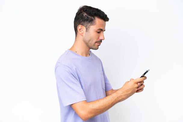 Jeune homme beau sur fond blanc isolé envoyer un message ou un e-mail avec le mobile - Photo, image