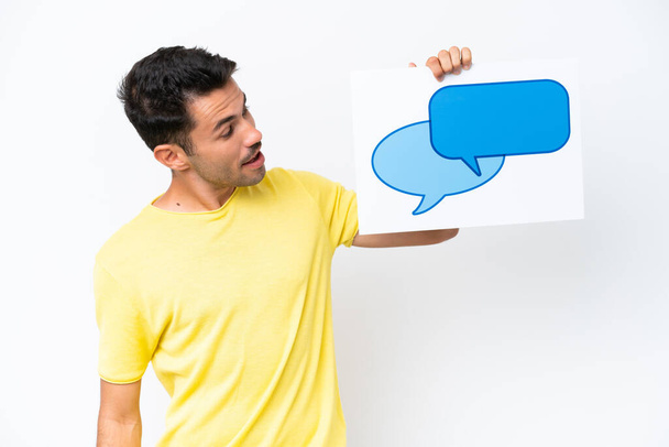 Young handsome man over isolated white background holding a placard with speech bubble icon - Foto, Imagem