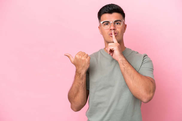 Young caucasian handsome man isolated on pink background pointing to the side and doing silence gesture - Photo, Image