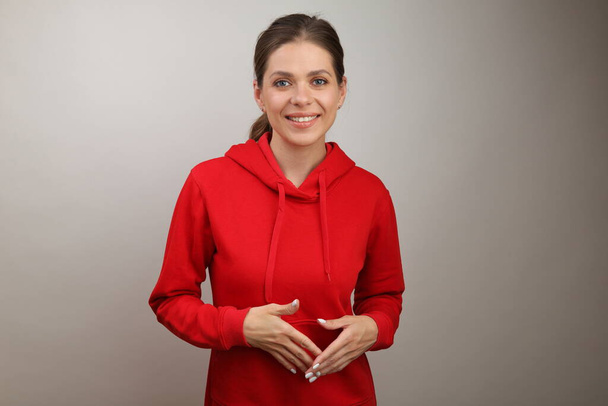 Smiling girl in red hoodie standing with folded hands. isolated studio female portrait. - 写真・画像