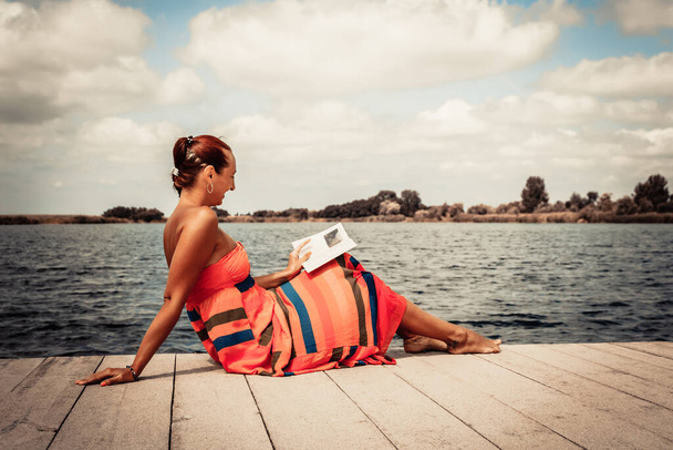 Щаслива жінка відпочиває на пірсі і читає книгу в літній день на пляжі
.  - Фото, зображення