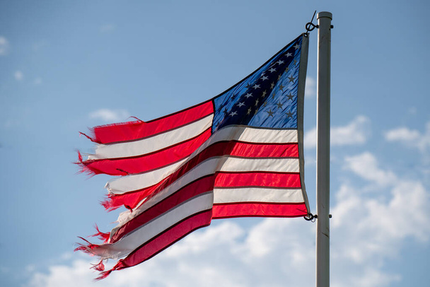 Tattered American flag against blue sky with white clouds in rural Minnesota USA - 写真・画像