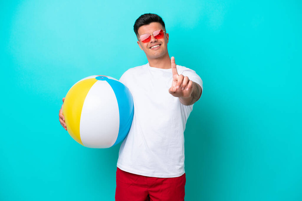 Молодий білий чоловік тримає пляжний м'яч ізольований на синьому фоні, показуючи і піднімаючи палець
 - Фото, зображення