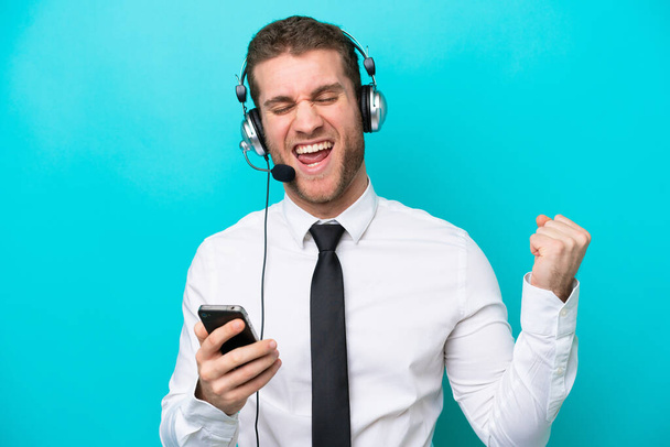 Telemarketer caucasian man working with a headset isolated on blue background with phone in victory position - Valokuva, kuva