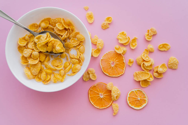 vista superior de naranjas secas cerca del tazón con hojuelas de maíz y leche orgánica en rosa  - Foto, Imagen