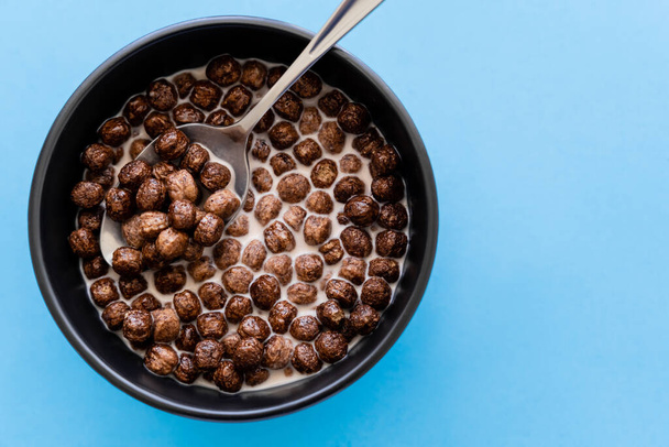 top view of tasty chocolate cereal balls in bowl with milk and spoon isolated on blue - Фото, изображение