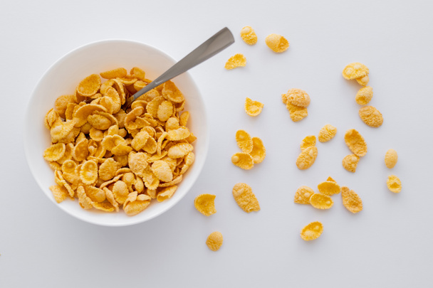 top view of bowl with crispy corn flakes and spoon isolated on white - Φωτογραφία, εικόνα