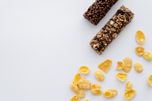 bovenaanzicht van knapperige cornflakes in de buurt van smakelijke granola bars geïsoleerd op wit  - Foto, afbeelding
