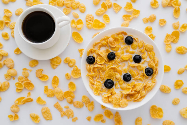 top view of bowl with corn flakes and milk near cup of black coffee isolated on white  - Photo, Image