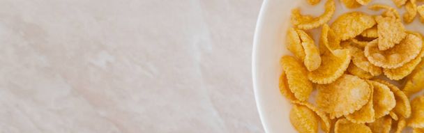 вид сверху на хрустящие кукурузные хлопья в миске с ложкой и молоком на мраморной поверхности, баннер - Фото, изображение