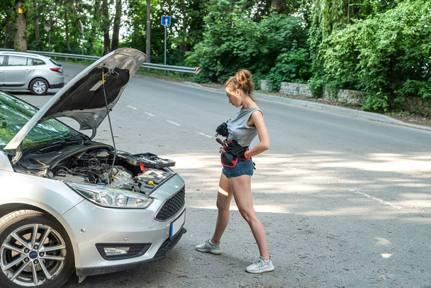 Beautiful young woman open hood and fixing the car on the roadside.  broken-down auto - Фото, изображение