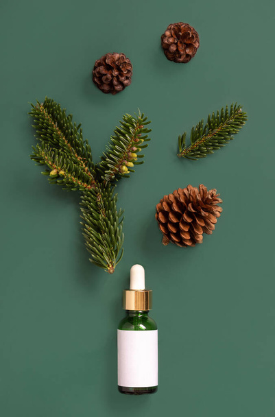 Green Pipette Dropper Bottle near fir branches and pine cones on green top view. Brand packaging mockup. Skincare beauty product, cream or serum. Healthcare natural cosmetics  - Foto, immagini