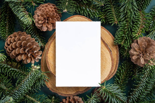 Vertical blank card between fir branches and pine cones on green top view, mockup. Christmas or New Year greeting card template, Holiday winter composition - Fotoğraf, Görsel