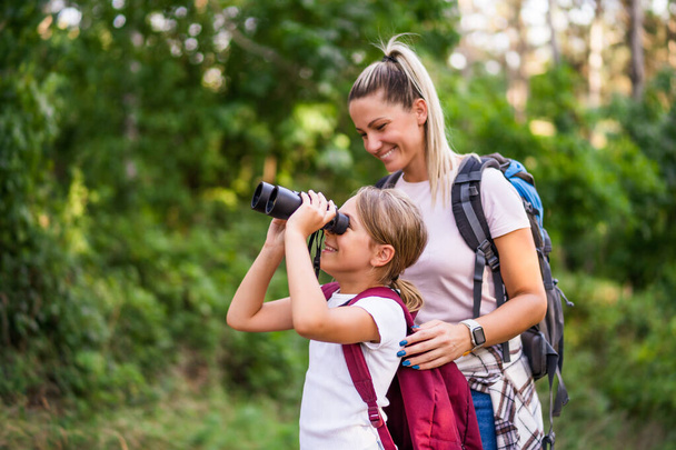 Mother and daughter using binoculars and enjoy hiking together. - Фото, зображення