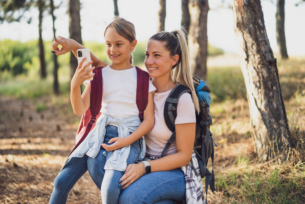 Mother and daughter are  taking pictures with phone while enjoy hiking. - Foto, imagen