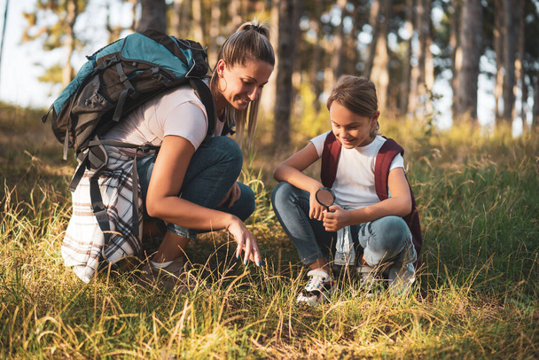 Mother and daughter  explore with magnifying glass nature while hiking. - Foto, imagen