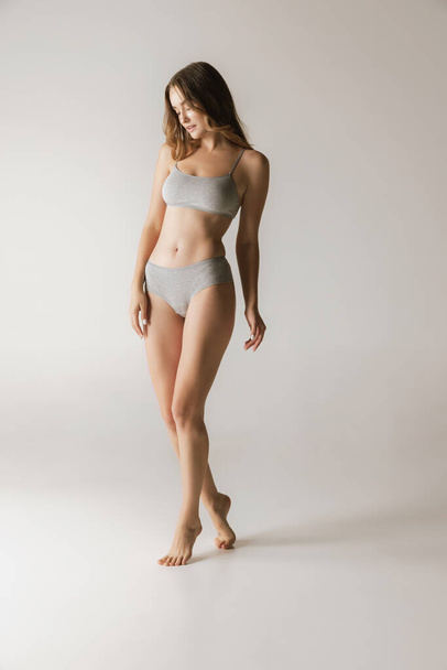 Femininity. Young beautiful slim woman in grey cotton underwear isolated over gray background. Wellness, wellbeing, fitness, diet and aesthetic cosmetology concept. Natural beauty of female body - Φωτογραφία, εικόνα