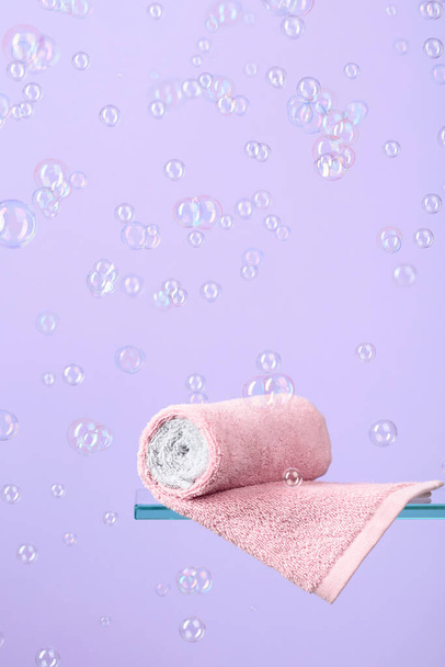 Handtuch auf einem Glasregal. Violet Hintergrund mit Blasen. Konzept des Themas Bad und Hygiene. Kopierraum. - Foto, Bild