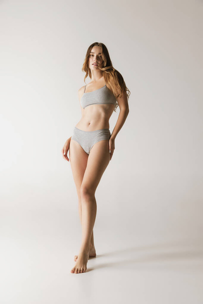 Femininity. Young beautiful slim woman in grey cotton underwear isolated over gray background. Wellness, wellbeing, fitness, diet and aesthetic cosmetology concept. Natural beauty of female body - Fotografie, Obrázek